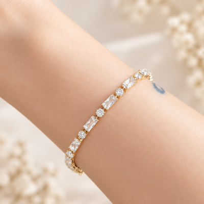 Pulseira dourada com pedras transparentes no pulso de uma pessoa.