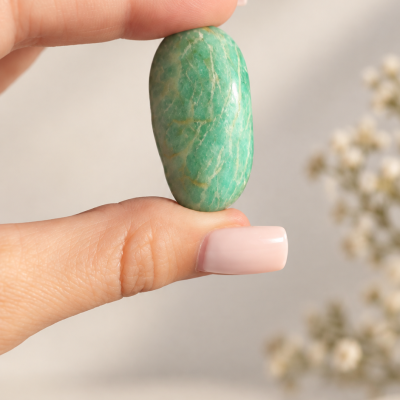 Pedra verde polida segurada entre dedos femininos com unhas rosa claro