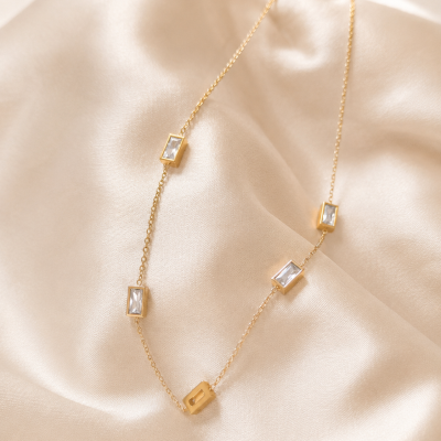 Colar dourado com cristais retangulares sobre tecido bege