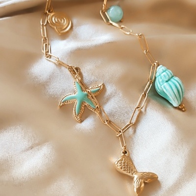 Colar dourado com pendentes marinhos sobre tecido bege