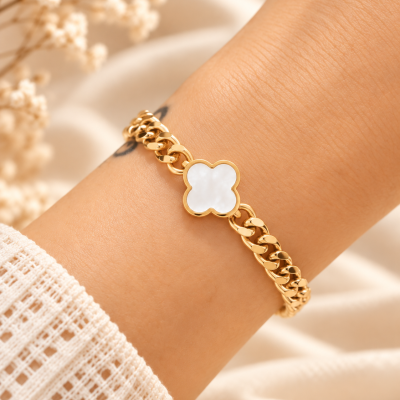 Pulseira dourada com pendente branco em forma de flor no pulso