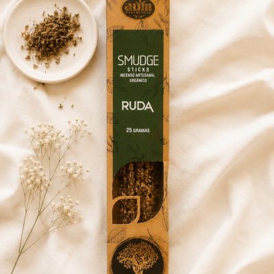 Incenso artesanal Smudge Sticks Ruda com embalagem em papel castanho e verde junto a ruda seca e flores brancas sobre tecido bege.
