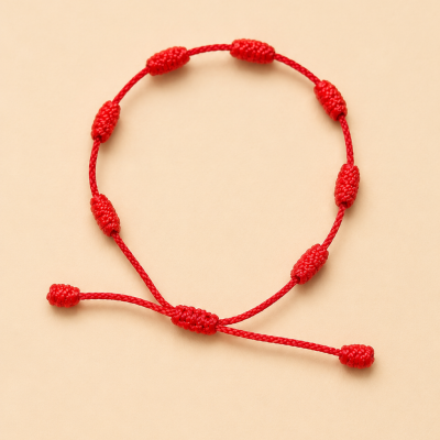 Pulseira de corda vermelha com nós decorativos em fundo bege