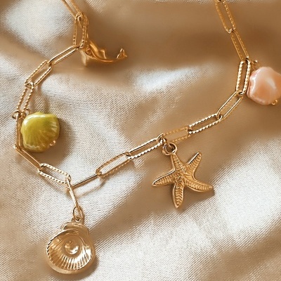 Colar dourado com pendentes em forma de conchas e estrela do mar sobre tecido bege.