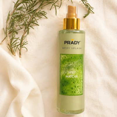 Frasco de body splash Prady Very Matcha com tampa dourada sobre tecido branco e ramo verde