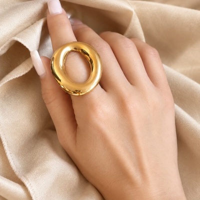 Mão feminina com anel oval dourado grande sobre tecido bege