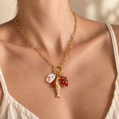 Colar dourado com pendentes coloridos em formato de peixe, tomate e pingente branco usado num pescoço com blusa branca