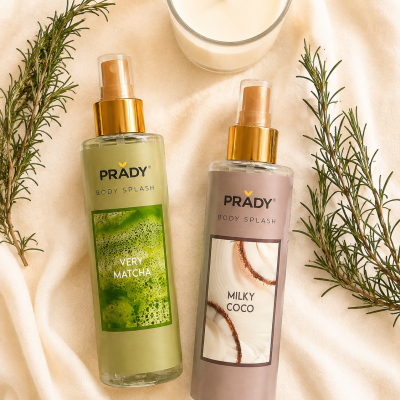 Dois frascos de spray corporal PRADY VERY MATCHA e MILKY COCO sobre tecido bege com ramos verdes e vela branca