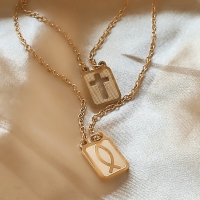 Colar dourado com pingentes religiosos sobre tecido branco