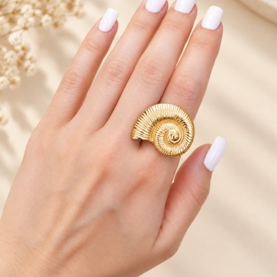 Anel dourado em espiral com textura, usado numa mão com unhas brancas