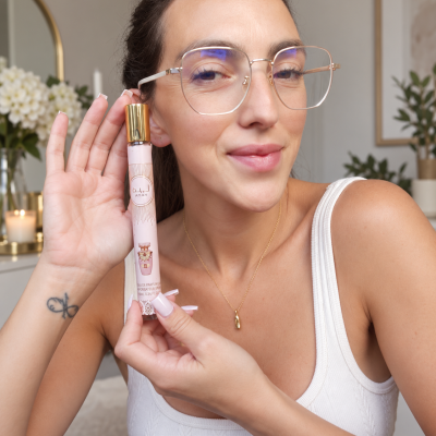 Mulher segurando frasco de perfume rosa com tampa dourada