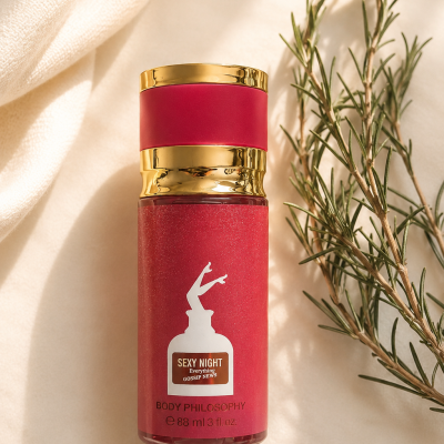 Frasco de perfume vermelho e dourado com rótulo branco e texto visível colocado sobre tecido claro com ramo verde