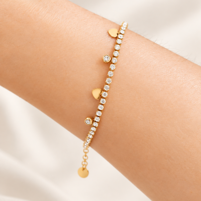 Pulseira dourada com pedras e pendentes em forma de coração no pulso