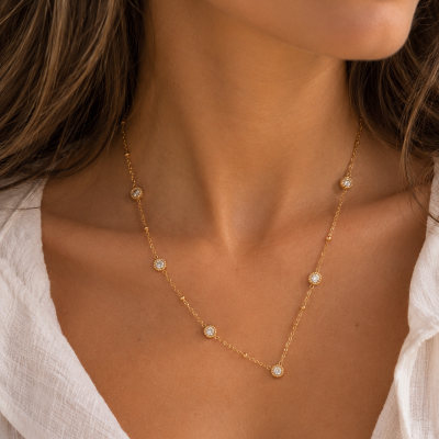 Colar dourado com pedras transparentes no pescoço de mulher com camisa branca