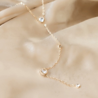 Colar dourado com pedras transparentes sobre tecido bege acetinado