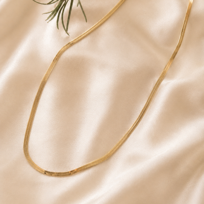 Colar dourado de corrente fina sobre tecido acetinado bege