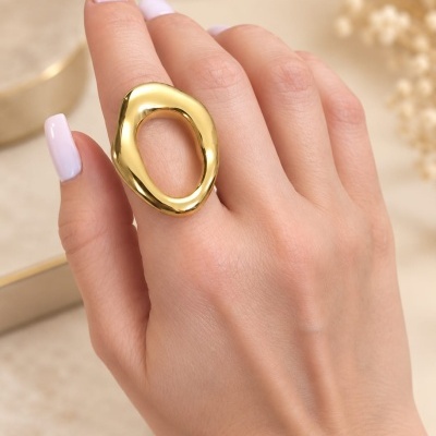 Anel dourado oval aberto numa mão com unhas brancas peroladas