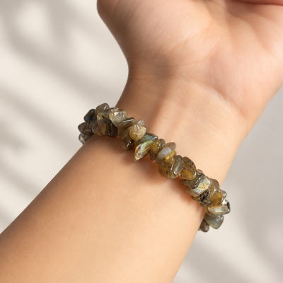 Pulseira de pedras verdes e azuis num pulso com unhas rosa claro.