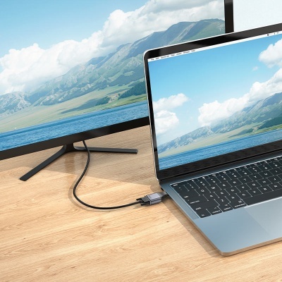 Computador portátil cinzento com monitor externo preto e cabo USB-C numa mesa de madeira