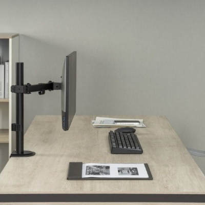 Mesa de escritório com monitor, teclado e tablet, cadeira cinza e estante com livros ao fundo