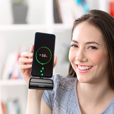 Mulher segura smartphone a carregar num suporte preto com marca hoco.