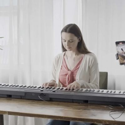 Mulher a tocar teclado digital KORG com smartphone num suporte