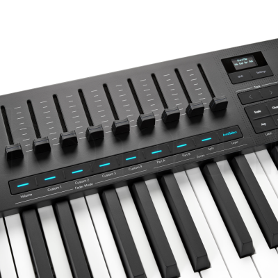 Teclado MIDI preto com botões, sliders e ecrã digital pequeno