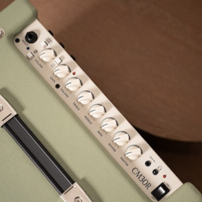 Amplificador de guitarra verde claro com painel branco e botões rotativos em superfície castanha
