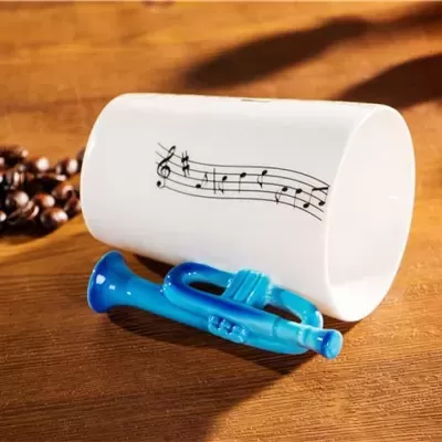 Caneca branca com pauta musical e mini trompete azul numa mesa de madeira