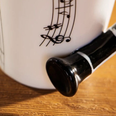 Caneca branca com padrão de notas musicais e alça preta sobre madeira