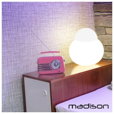 Rádio portátil cor-de-rosa sobre mesa de madeira e abajur branco