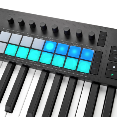 Teclado MIDI com pads iluminados azuis e verdes e botões rotativos pretos