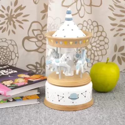 Carrossel musical infantil em madeira com cavalinhos brancos e azuis e base decorada ao lado de maçã verde e livros
