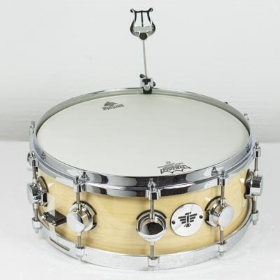 Tambor de madeira clara com aros cromados e pele branca com logótipos Remo e PDP