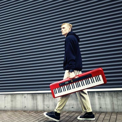 Rapaz com teclado musical vermelho a andar junto a parede metálica