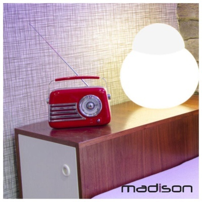 Rádio portátil vermelho com antena em móvel de madeira ao lado de lâmpada redonda acesa