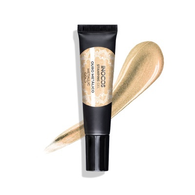 Bisnaga preta de produto com rótulo branco e bege, texto INOCOS, sobre textura dourada cremosa.