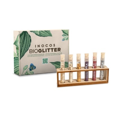 Conjunto de glitter biodegradável INOCOS BIOGLITTER com tubos em suporte de madeira e caixa decorativa com folhas verdes.