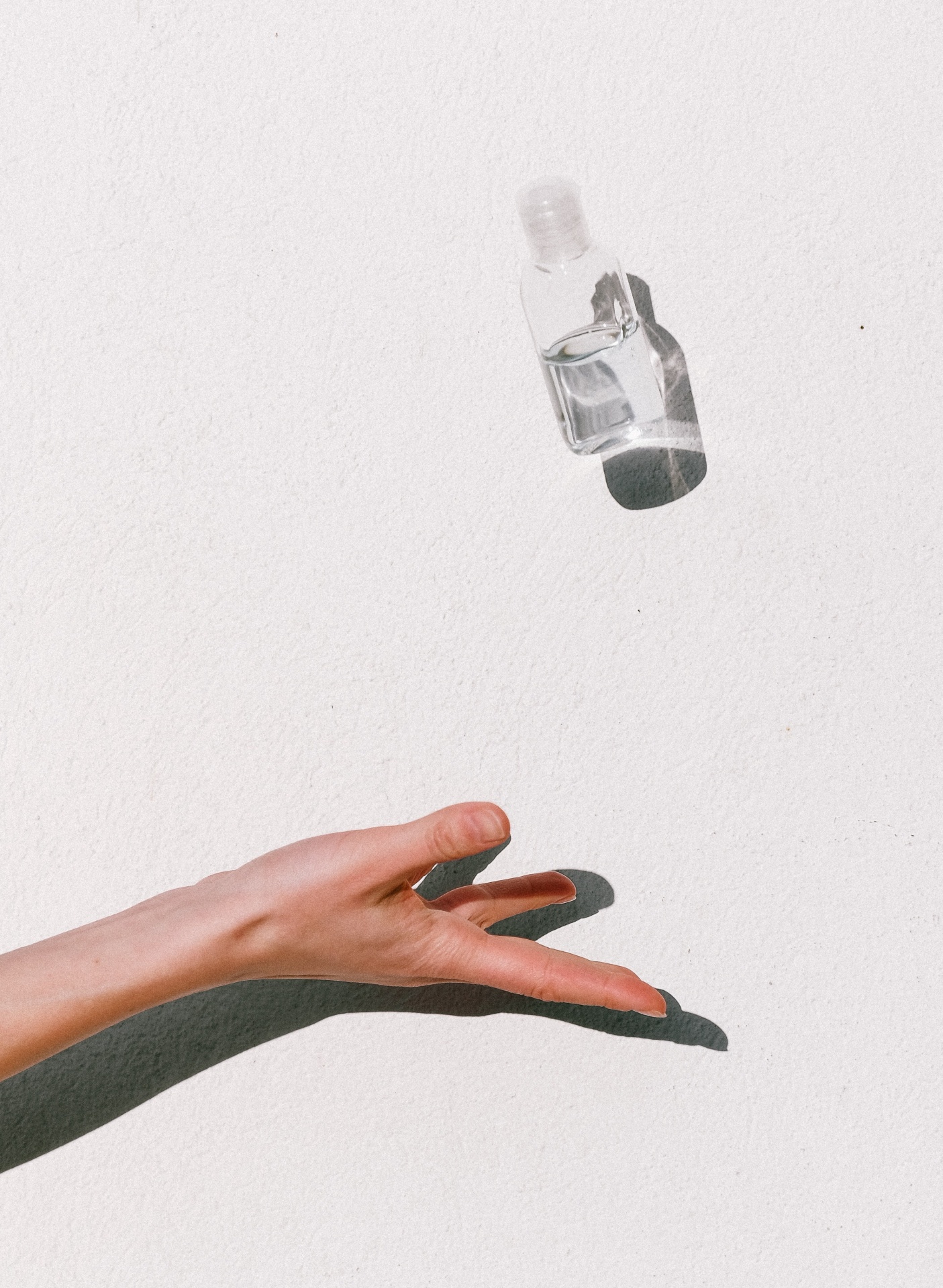 Mão estendida e frasco transparente com líquido, sombra em fundo branco.