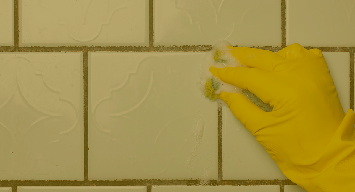 Mão com luva amarela limpa azulejos brancos com esponja verde e branca