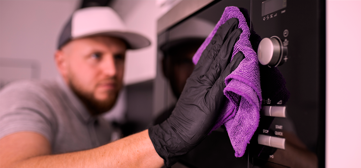7 dicas de como limpar eletrodomésticos de cozinha Pessoa a limpar eletrodoméstico com pano roxo e luvas pretas