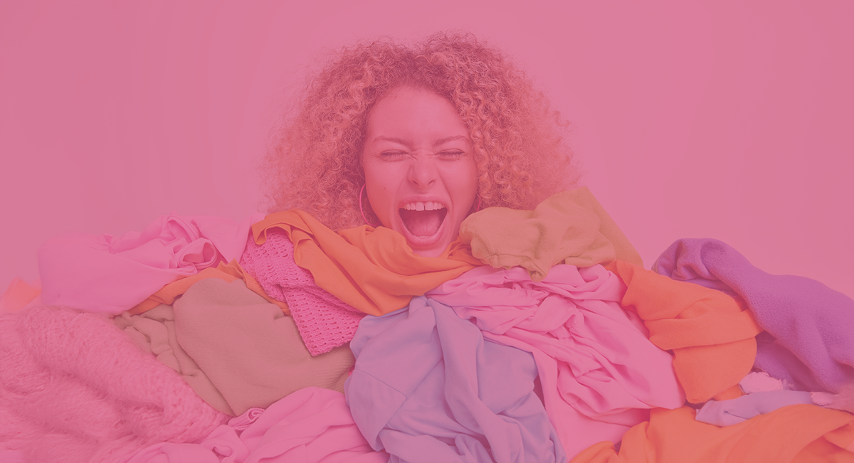 Mulher sorridente rodeada por roupas coloridas em fundo rosa