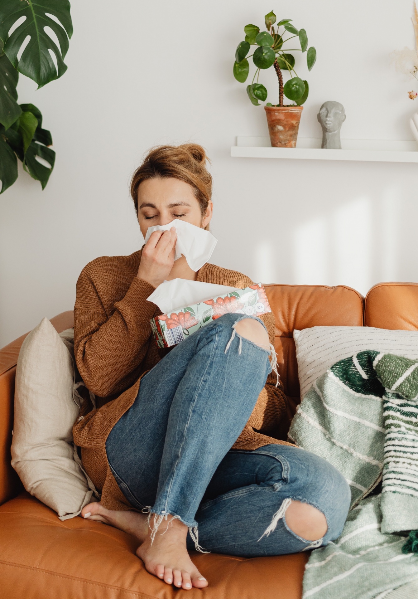 Mulher numa sala sentada num sofá a usar lenço com caixa de lenços.