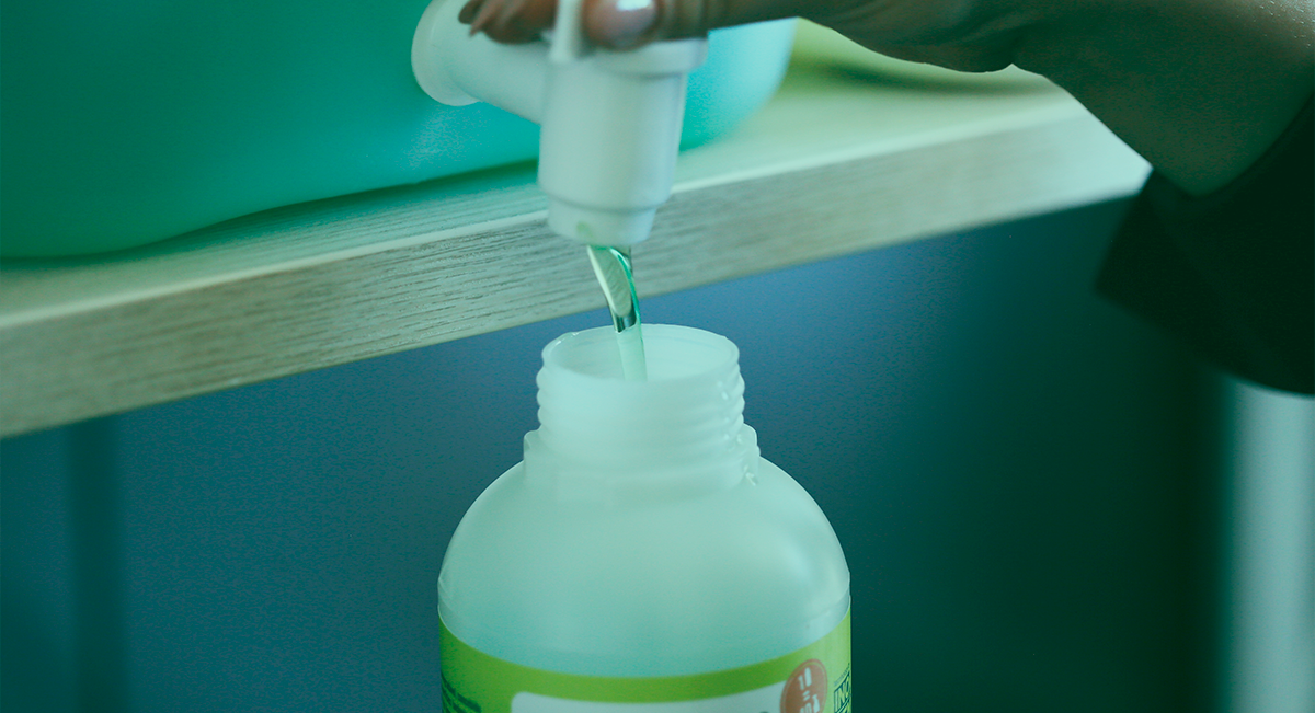 Mão a verter líquido verde de frasco branco em recipiente sobre superfície de madeira