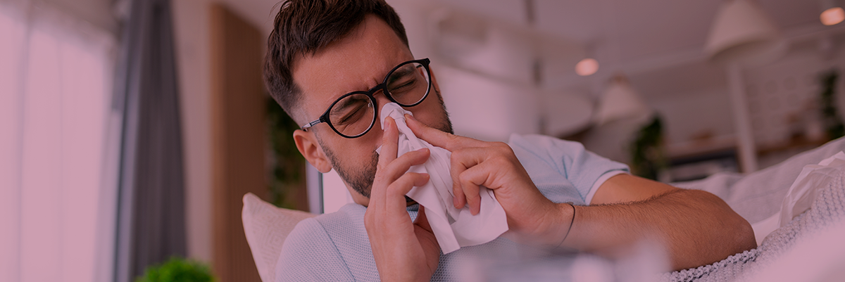 Homem a assoar o nariz com um lenço branco sentado num sofá num ambiente moderno