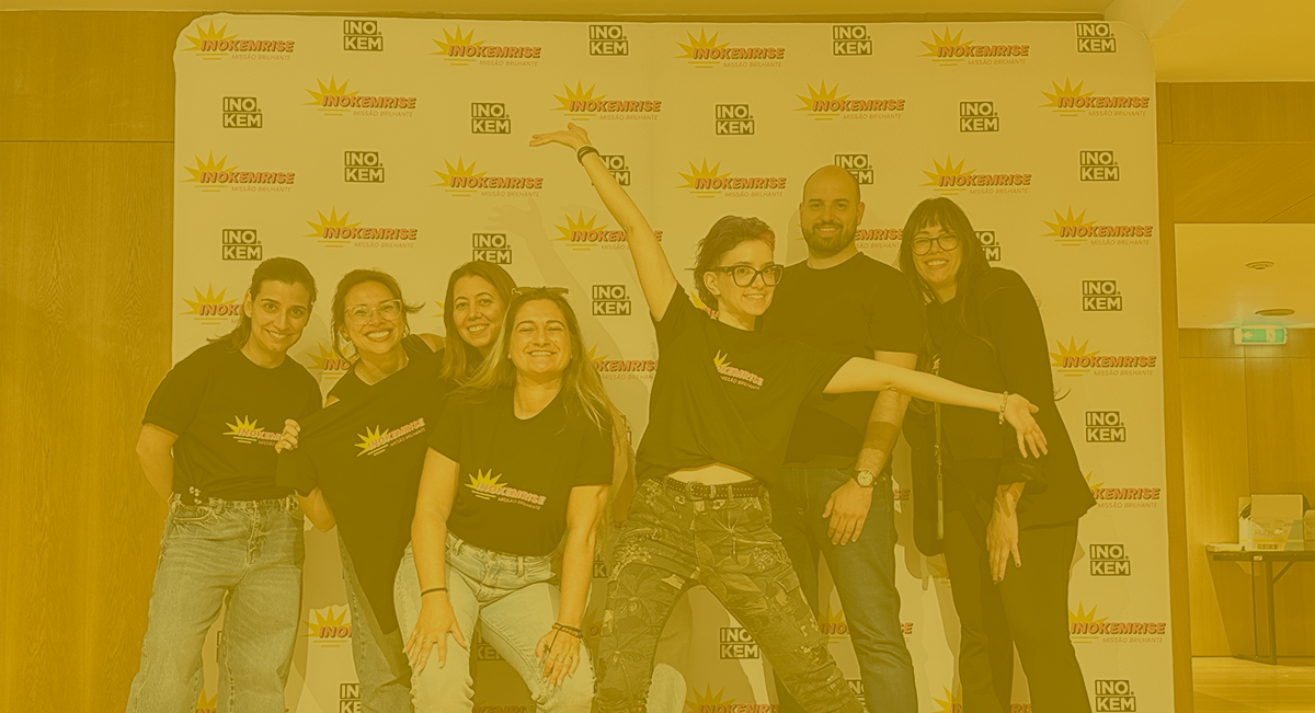 INOKEMRISE: Uma missão brilhante ✨ Grupo de sete pessoas com t-shirts pretas posam em frente a fundo publicitário com logotipos.
