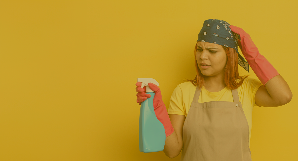 Mulher com avental e luvas segurando frasco spray azul com fundo amarelo