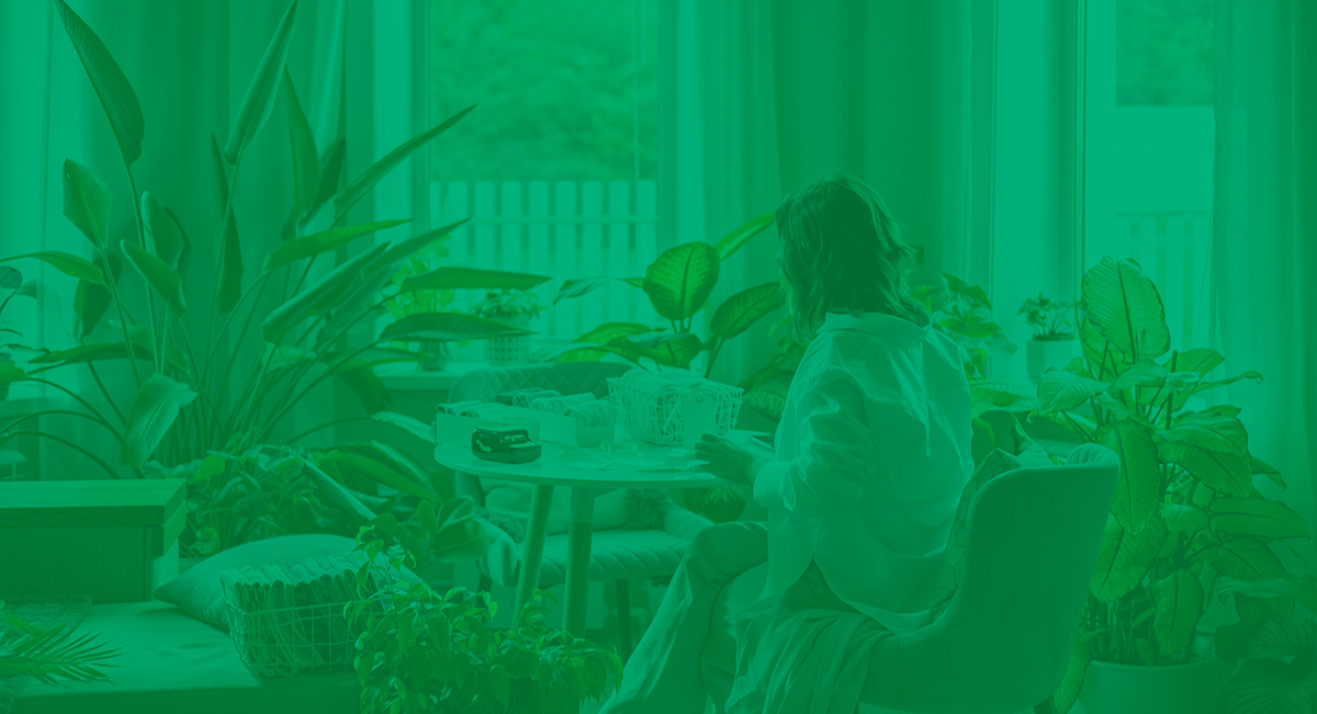 Como adotar uma vida mais sustentável: 6 dicas para começar hoje! Pessoa sentada numa sala cheia de plantas verdes junto a uma mesa redonda branca