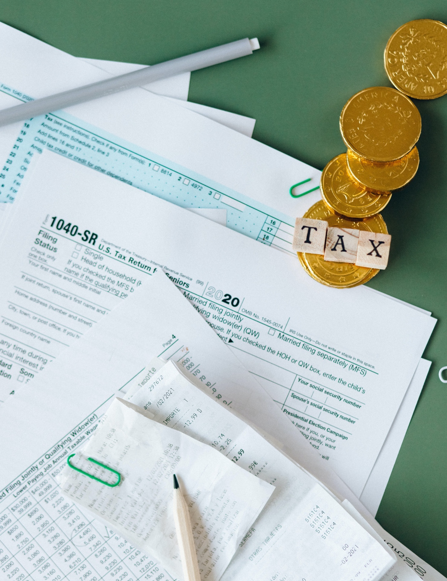Formulário fiscal 1040-SR, moedas douradas com blocos a formar a palavra TAX, canetas e clips verdes sobre fundo verde