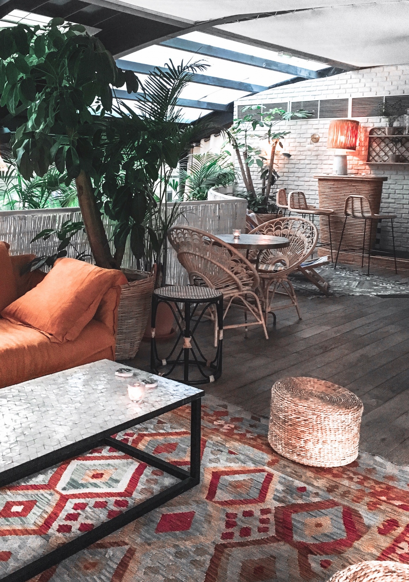 Sala com sofá laranja, mesa de centro marmoreada, cadeiras em rattan e tapete colorido